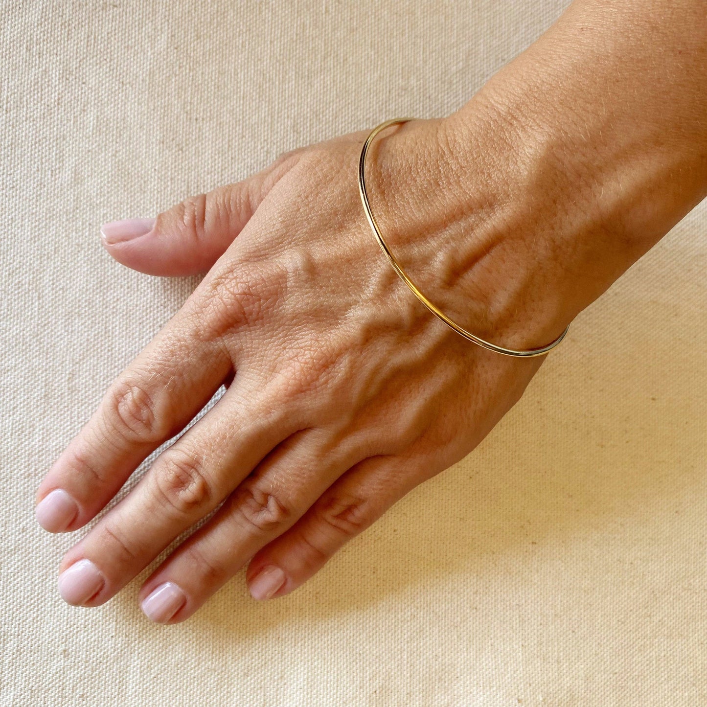 Hand wearing gold bangle bracelet on a beige background