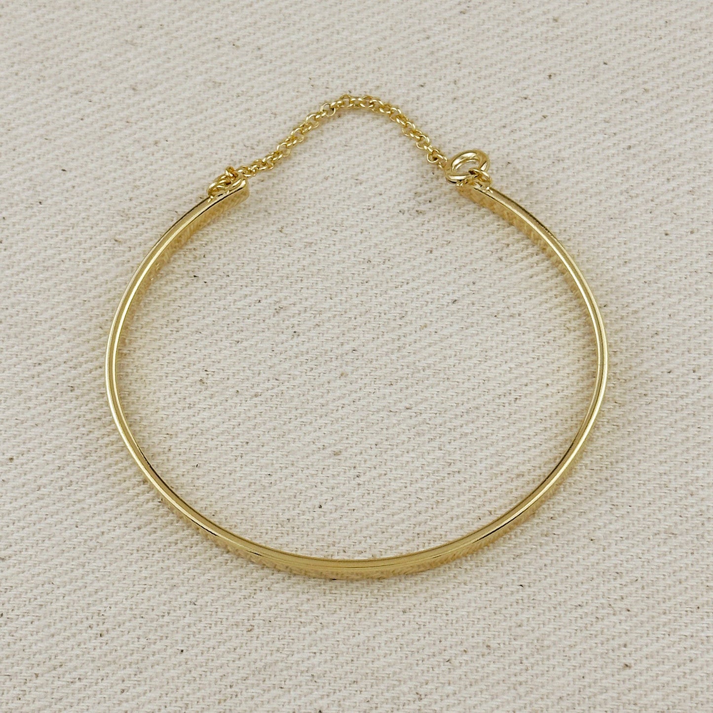 Gold bangle bracelet with chain on a beige background