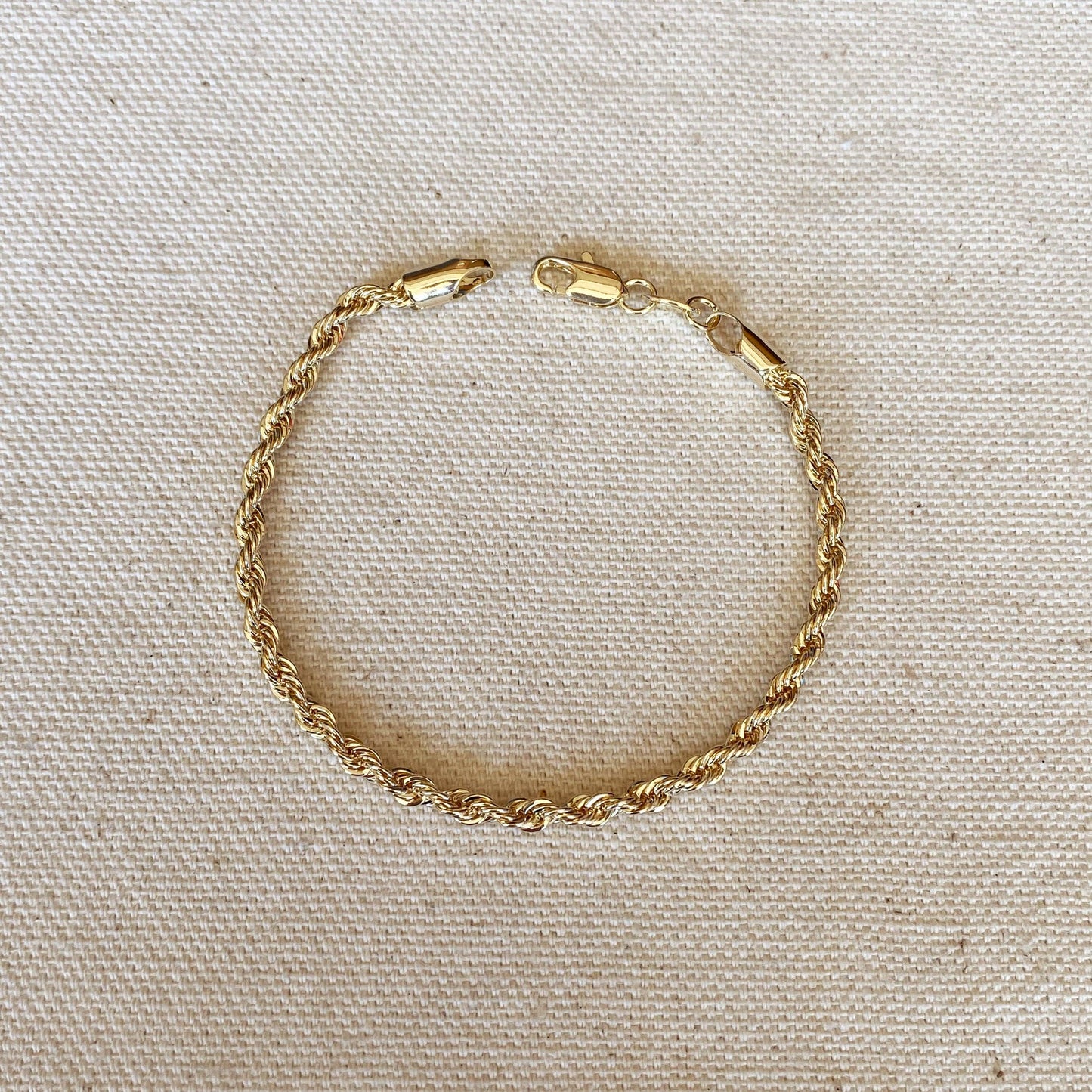 An 18k gold filled braided rope bracelet featuring a lobster clasp, shown close up.