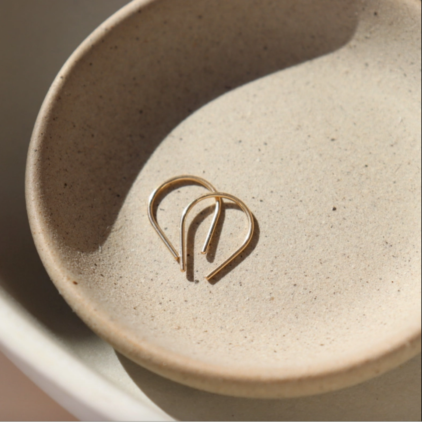 Minimal horseshoe ear wire earrings in gold filled on ceramic dish