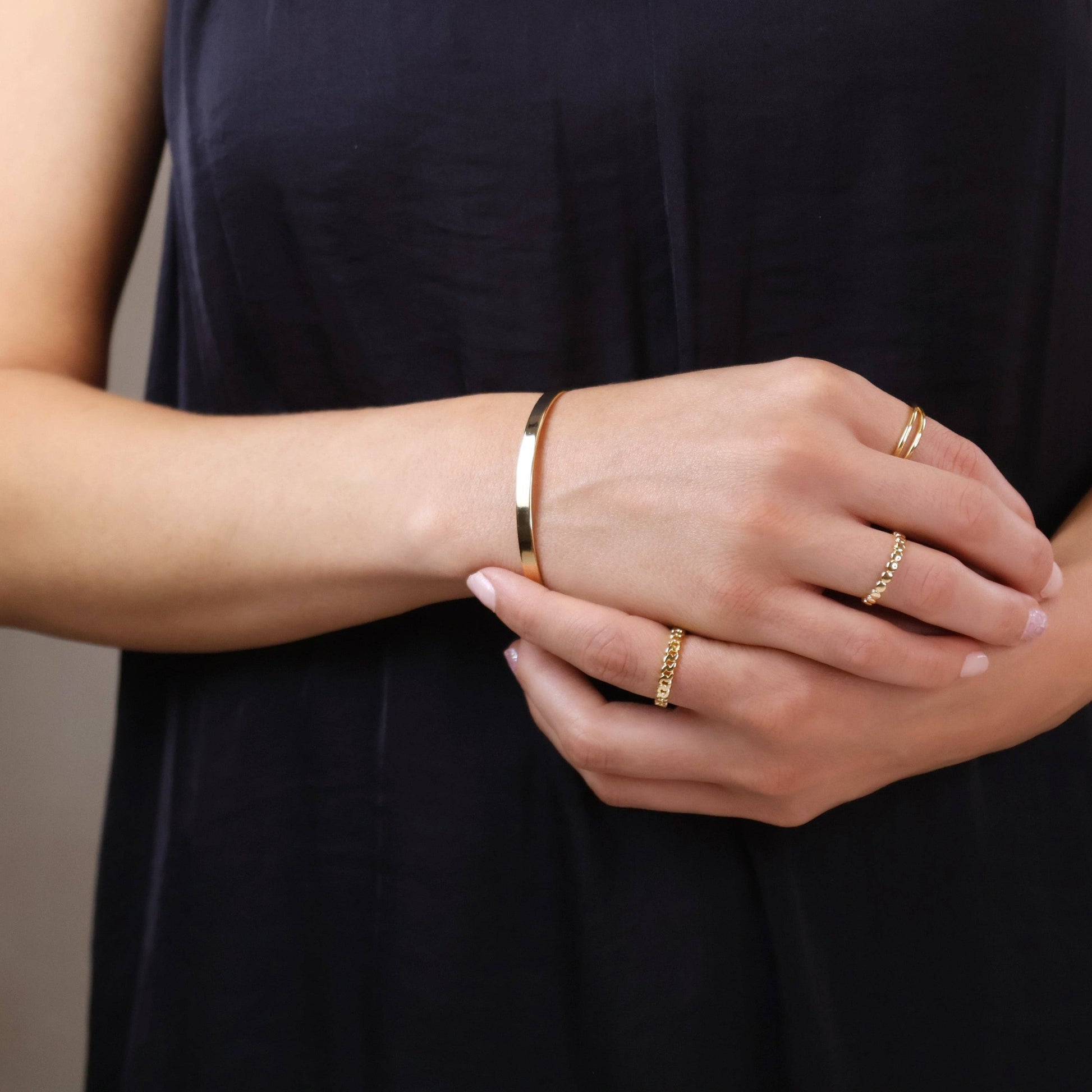 Close up of woman wearing gold bangle bracelet and gold rings