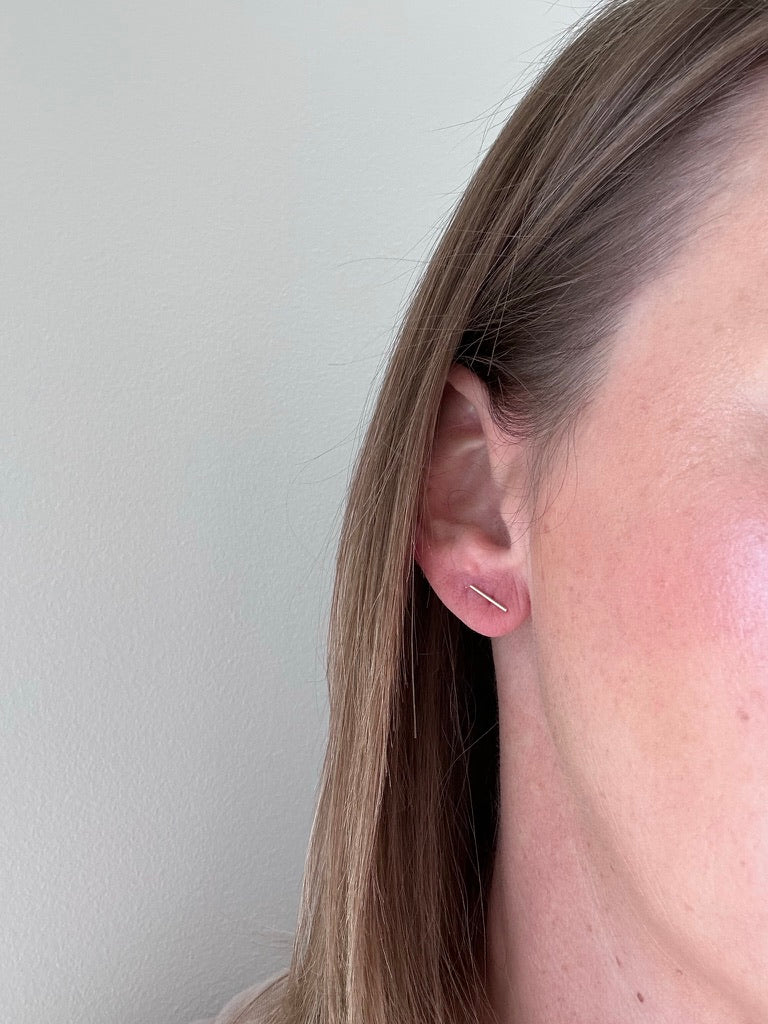 Tiny bar stud earrings in sterling silver shown on woman's ear